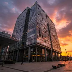 Imagen 3 — A modern glass skyscraper reflecting clouds at sun