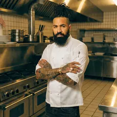 Recraft V4 — A tattooed chef in a white coat, arms crossed, con
