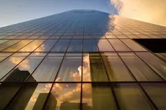 Reve v1.0 — A modern glass skyscraper reflecting clouds at sun