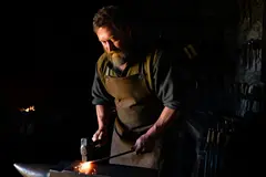 Reve v1.0 — A bearded blacksmith in a dark workshop, sparks fl