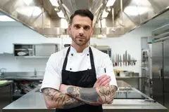 Reve v1.0 — A tattooed chef in a white coat, arms crossed, con
