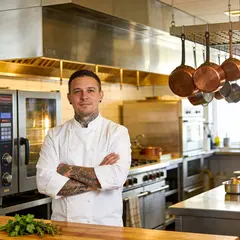 Seedream v4.5 — A tattooed chef in a white coat, arms crossed, con