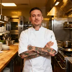 Seedream v4 — A tattooed chef in a white coat, arms crossed, con